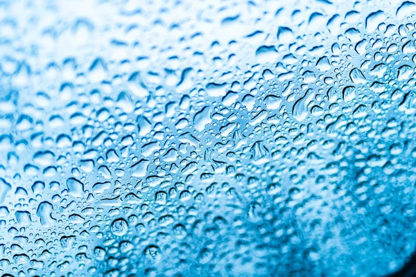 Rain drops on the glass window on blue background. Blue drops on glass after the rain. Close-up