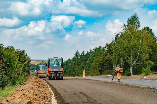 Yol yapımı silindir kompaktör makine ve asfalt finisher ile yaz aylarında güzel doğa arka plan üzerinde çalışıyor. Yeni asfalt yolun alt ve özel teknik döşeme.