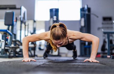 Güzel kız şınav yerden eğitim spor spor malzemeleri arka plan üzerinde elinde kasları için yapar. Sporcumuz at kuyruğu saç ile kas eğitimi yapıyor