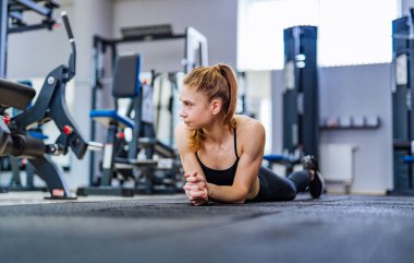 Yerde yatarken ve spor kulübü, mide egzersizleri yapıyor genç kadın uygun. Genç kadın rahatlatıcı bir bakışla ciddi dalgın bir kenara bir spor salonunda bir çalışmadan sonra yorgun.