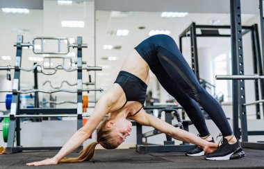 Yan görünümü atış fitness de şekilli kadın köpek gerçekleştirme orta bacağını spor salonu zemin dokunmadan el ile poz. Alt sırt ve omurga germe