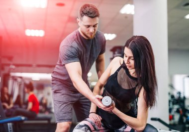 Spor salonunda, o dumbbells ile egzersiz genç bir kadın yardım kişisel fitness eğitmeni.
