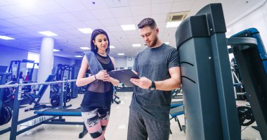 Kişisel antrenör ve onun ilerleme salonunda bakarak istemci. Atletik erkek ve kadın giyim spor giyim.