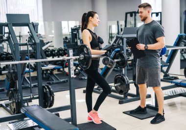 Kişisel antrenör ve onun ilerleme salonunda bakarak istemci. Atletik erkek ve kadın giyim spor giyim.