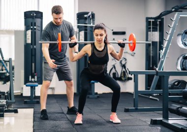 Young beautiful woman doing exercises with personal trainer. Beautiful girl squats under the supervision of the coach. clipart