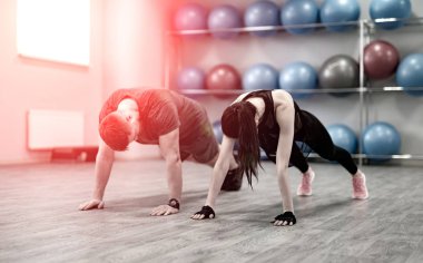 Sportif genç çift ışık sızıntıları ile spor salonunda şınav. Genç kadın ve erkek spor kulübü arka plan fitness topları stand ile eğitimde vardır.