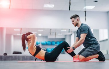 Kadının karın egzersizi basın egzersiz onu spor erkek antrenman ör içinde jimnastik salonu ile mindere yapması. Çift egzersizleri üzerinde arka plan bulanık spor salonu.