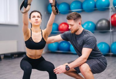 Çekici Bayan fitness merkezinde Trx ile uygulamaya yardımcı kas sakallı eğitmeni. Sportif kadın spor salonunda kişisel eğitmen ile yapıyor. Yakın çekim