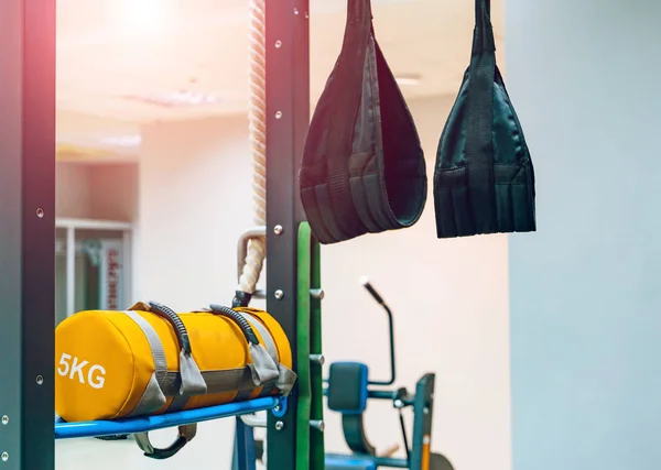 Training straps trx hanging from the wall and punching yellow bag with 5 kg in gym. Training equipments workout items for healthy and martial arts