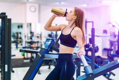 Spor salonunda sert çalışmadan sonra atletik genç kadın. Fitness kız sportif beslenme ile shaker tutar