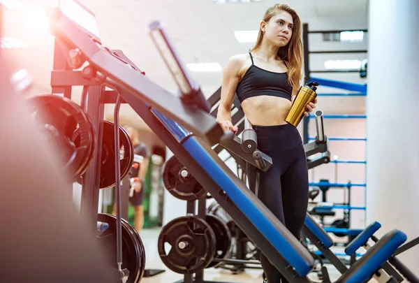 Belle fille athlétique habillée en haut de sport noir et collants avec shaker. Femme regardant le miroir après l'entraînement dans une salle de gym . — Photo