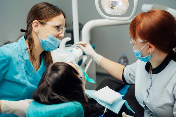 Assistenz- und Stomatologen-Frauen in Masken und Schutzbrillen arbeiten mit einer Patientin in einer Zahnarztpraxis. Kariesschutz. Karies-Behandlung — Stockfoto