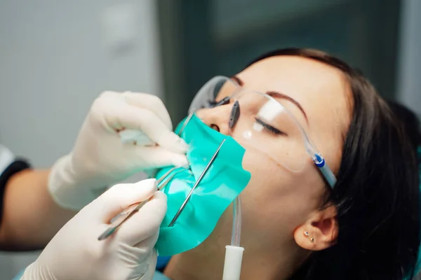 Pacjenta dziewczyna z ochrony okulary i usta zwijacza w trakcie leczenia, leżącego w gabinecie stomatologicznym. Gabinet stomatologiczny ręce w białych rękawiczkach pracy z pacjentka. Szczelnie-do góry — Zdjęcie stockowe