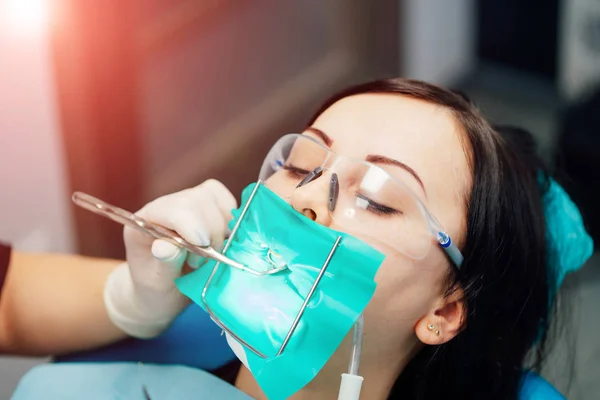 Schöne Patientin beim Zahnarztbesuch in einer Klinik für Stomatologie. Frau mit Schutzbrille in Zahnarztpraxis bekommt eine Oralbehandlung. Nahaufnahme — Stockfoto