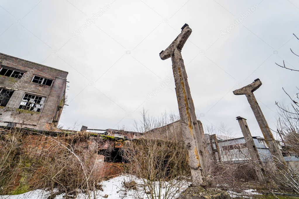 Remaining pillars of the destroyed buildings on the background of abandoned houses in winter. Ruined place in the city in collapse outdoors with some snow on the ground.