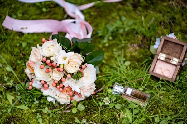 Wedding bouquet and rings lying down on green grass — Stock Photo, Image