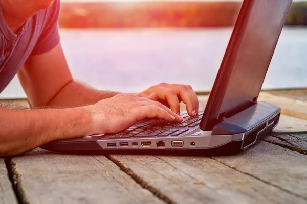 Menschenhände tippen im Sommer vor dem Hintergrund des Flusses Text auf einen Laptop. Nahaufnahme — Stockfoto