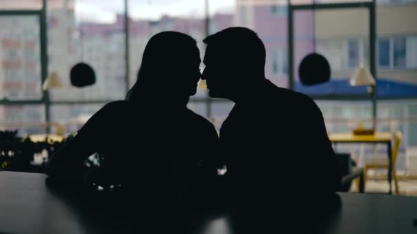 魅了された男と女のシルエットは 窓の背景にあるレストランでテーブルの上に互いの絡み合った手で飲み物を飲んでいる — ストック動画