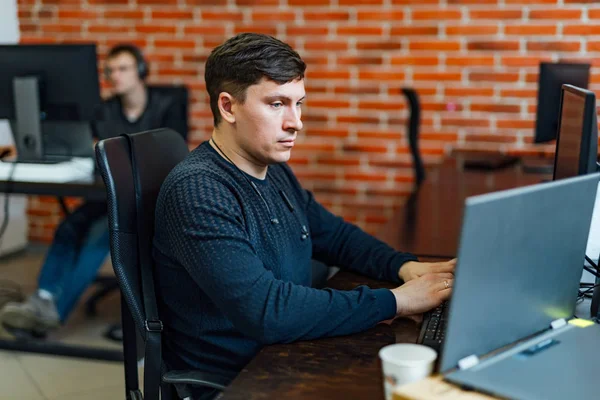 Joven ejecutivo sentado en su escritorio con portátil leyendo un docume —  Fotos de Stock