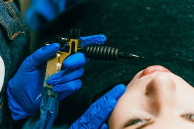 Bir güzellik mavi koruyucu eldiven eller kadının yüzüne dövme makinesi. Kalıcı makyaj Güzellik Salonu dudaklarında için. Yakın çekim