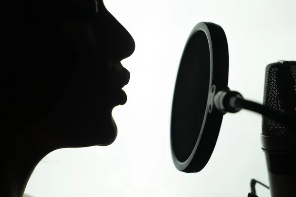 Perfil en blanco y negro de una joven cantando en el micrófono redondo. Primer plano de la cara de la hembra cerca del micrófono . —  Fotos de Stock