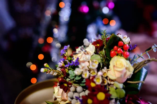 Pair of wedding rings lying on a colorful bouquet with different flowers over the blurred background. Romantic rings on flowers as bridal accessories — Stock Photo, Image