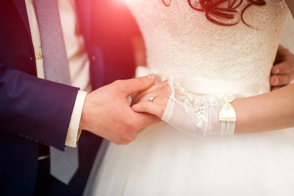 Primo piano di mani di coppia romantica che tiene insieme durante cerimonia nuziale. Elegante sposo tiene la mano della sposa con fede nuziale . — Foto Stock