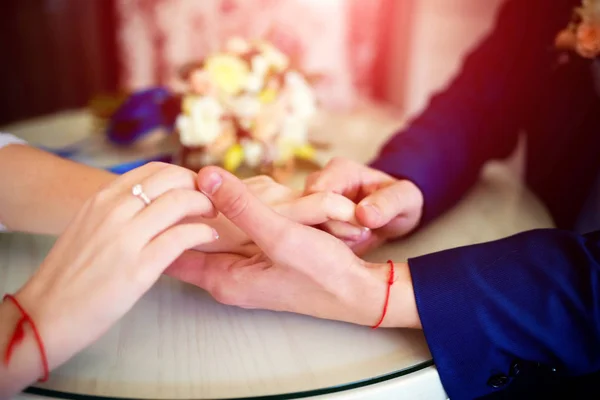 Sposa e sposo si tengono per mano con fedi nuziali sul tavolo sullo sfondo bouquet sfocato. Matrimonio coppia si tiene per mano. Primo piano — Foto Stock