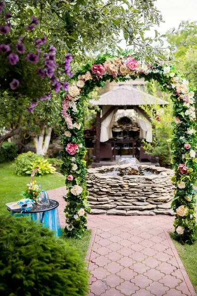 Romantické místo s květinovým obloukem a fontána v kameny v zahradě. Oblouk pro svatební obřad, květinovou výzdobou nad přirozené pozadí. — Stock fotografie