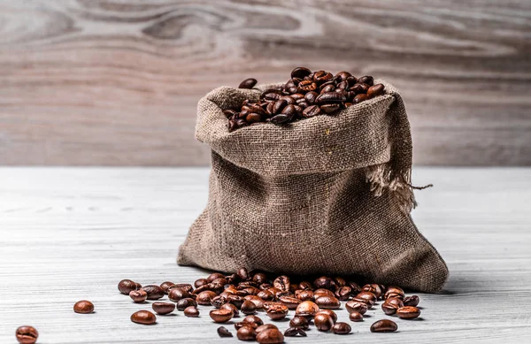 Kis zsákvászon zsák tele friss pörkölt Arabica bab és néhány magot feküdt az asztalra. Barna, természetes robusta szemszemek a fényfelületen. — Stock Fotó