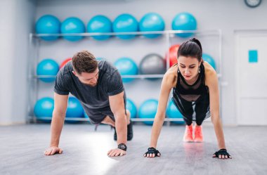 Sportif genç çift hafif fitness merkezinde şınav yapıyor. Güzel kadın ve yakışıklı adam topları standı arka plan ile spor kulübünde eğitim.