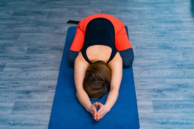 Kadının bedeni paspasın üzerine uzanmış, başı aşağıda ve antrenman sırasında dinleniyor. Spor kıyafetli genç bir bayan yoga yapıyor ve yoga stüdyosunda nefes egzersizi yapıyor..