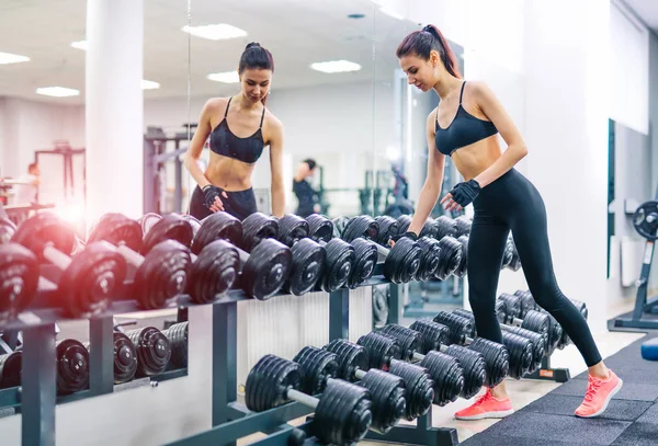 Schlanke sportliche Mädchen nimmt Hanteln, die vor dem Spiegel in der Turnhalle stehen. schönes Frauentraining im Sportzentrum. Konzept eines gesunden Lebensstils. — Stockfoto