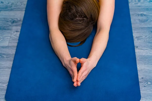 Крупним планом жіночі руки і голова роблять йогу на синьому килимку. Молода жінка практикує йогу, займається дихальними вправами в релаксації позу на підлозі . — стокове фото