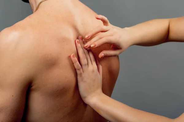 Close-up van het lichaam van de naakte man en de handen van de vrouw controleren terug. Dokters handen onderzoeken de man met rugpijn op de grijze achtergrond. — Stockfoto