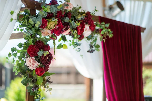 Hermosas flores decoradas en el arco de la boda en el fondo borroso. Diseño romántico de un arco de boda de tela y flores de color burdeos . — Foto de Stock