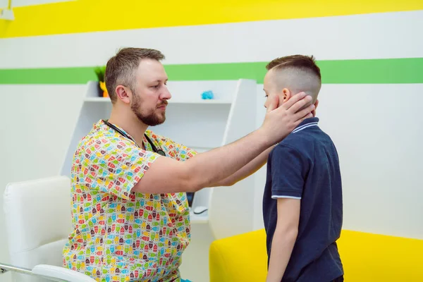 Un medico esperto sta guardando la gola del ragazzo in clinica. Il pediatra che esamina la gola del bambino. Medico in uniforme medica e un bambino . — Foto Stock