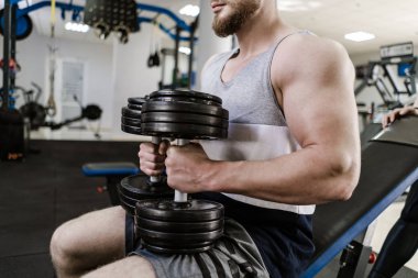 Spor salonunda ağır dambıl ile kas yakışıklı adam eğitim. Büyük pazıile genç adam oturur ve kapalı egzersiz yapar. Spor ve sağlık konsepti.