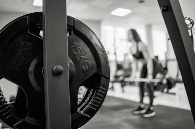 Spor salonunda eğitim alan bir kadının arka planında demir barbell diski. Barbell diskinde 15 kg. Close. Siyah beyaz fotoğraf.