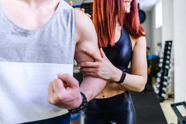 Close-up do bíceps do homem e da mulher segurando o braço do macho dentro de casa. Corpo muscular de um homem e fêmea magra. Fitness e conceito saudável . — Fotografia de Stock