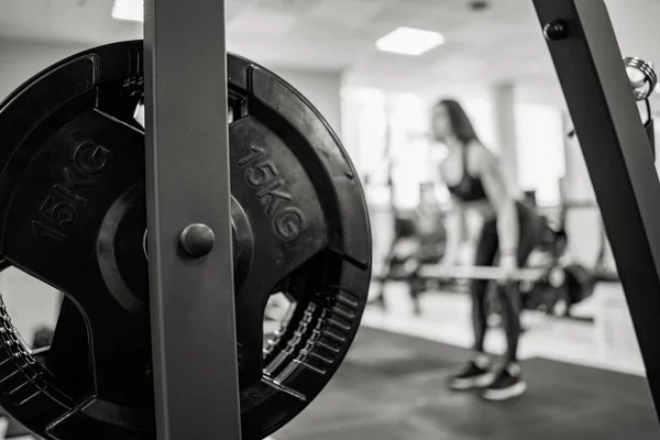 Spor salonunda eğitim alan bir kadının arka planında demir barbell diski. Barbell diskinde 15 kg. Close. Siyah beyaz fotoğraf. — Stok fotoğraf