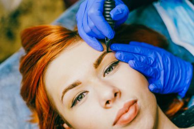 Dövme salonunda kalıcı kaş makyajı yapılan genç bir kadın. Güzellik uzmanı kalıcı kaş makyajı yapıyor. Güzellik tedavisi