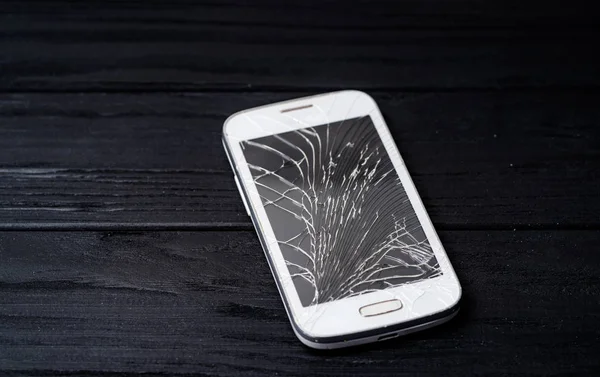 Smartphone with broken screen on dark background. Close-up.