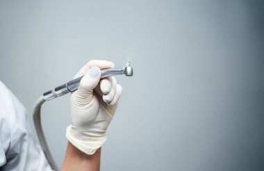 Dişçinin elindeki beyaz eldiven, bor makinesini tutuyor. Işık kliniğinin arka planında diş hekimi aleti. Close.