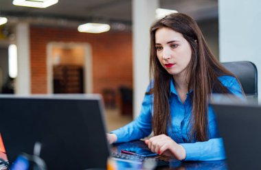 Konsantre kadın geliştirici modern ofiste bir bilgisayar üzerinde çalışıyor. Çekici genç kadın programcı bilişim şirketinde yeni teknolojiler geliştiriyor. Yüksek kaliteli resim.