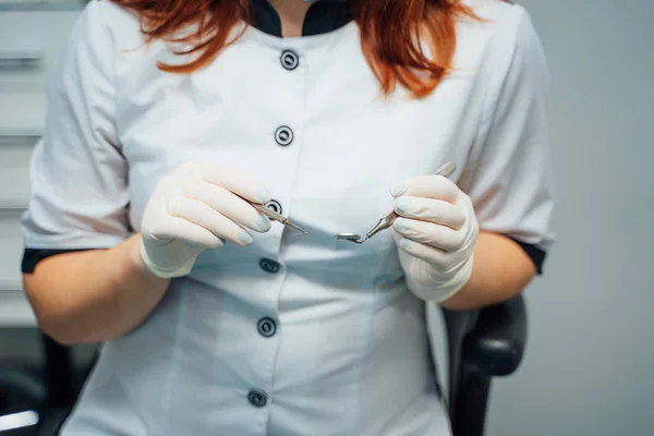 Mujer dentista con guantes médicos sosteniendo instrumentos médicos en la clínica. Equipos médicos inoxidables para clínica dental en manos del estomatólogo . —  Fotos de Stock