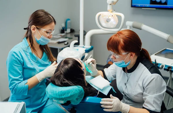 女性の歯科医とマスクと患者の歯を治療する保護眼鏡の看護師。歯科医院でのアシスタントを持つ医師の胃科医。胃学とヘルスケアの概念. — ストック写真
