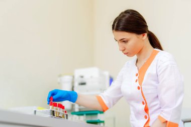 Tıp üniformalı güzel laboratuvar teknisyeni kadın kan örnekleriyle çalışıyor. Kadın araştırmacı laboratuvarda bir sürü sıvı şişesiyle çalışıyor..