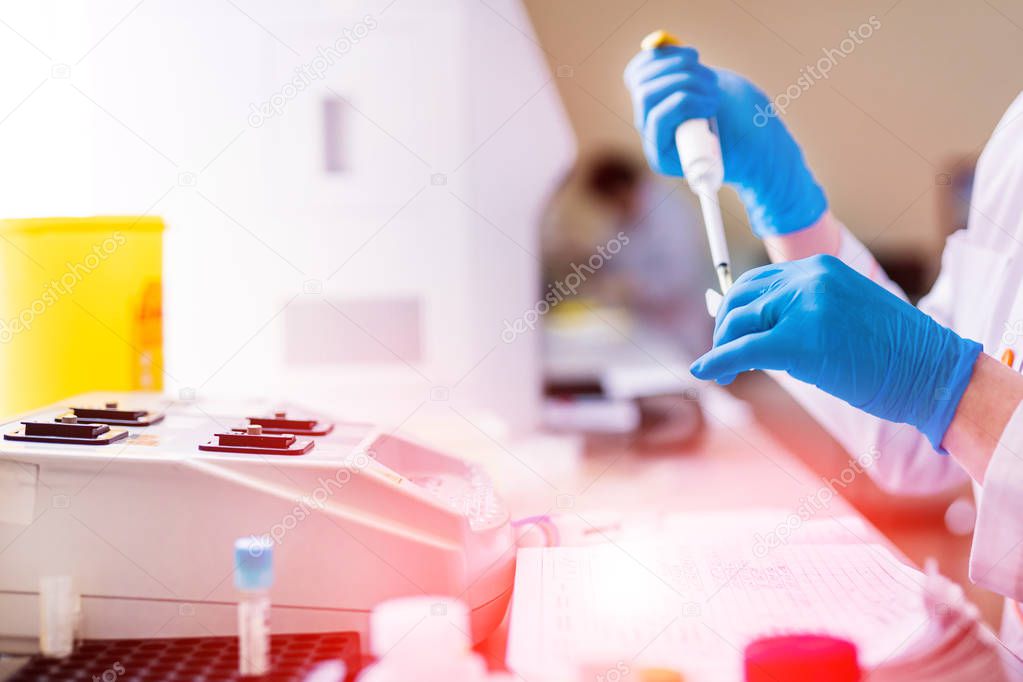 Professional laboratory technician fills vial with liquid and puts in the rack. Medical workers with test tubes of blood sample in the laboratory.