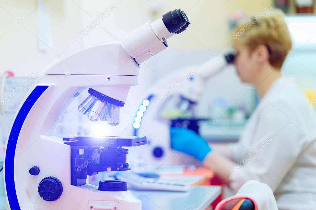 Modern microscopes and a laboratory specialist is looking at one of them indoors. Microscope plate laboratory is doing microscopic tests science research.